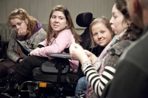 Four girls in wheelchairs, listening to an older one speak. they are very focused.