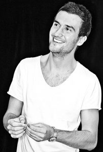A black and white photo of Grant Anderson. He is looking to the side, he has short brown hair and is smiling. 