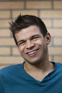 A photo of Robert Softley Gale. He has brown hair that is spiked up at the front and a big smile