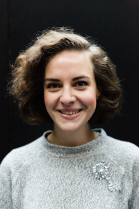 A photo of Cara Ballingall. She has short, curly brown hair and is smiling. 