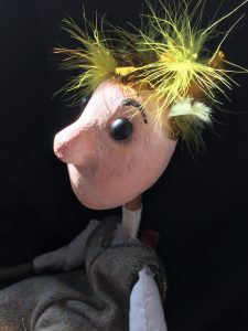 A photo of a small puppet with sparse blonde hair in a blue dress.