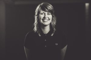 A black and white photo of Audrey Tait. She has feathery brown hair and a big smile. 