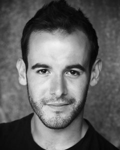 A black and white photo of Joseph Brown. He has short dark hair and some facial stubble.