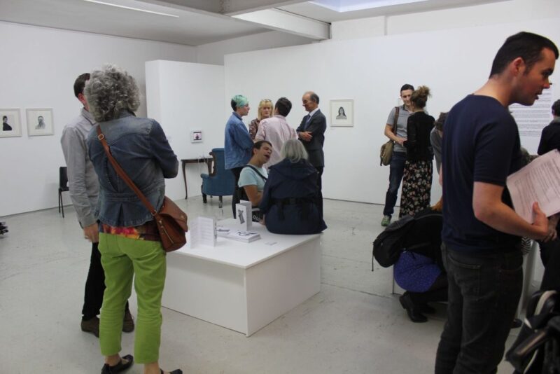 Clusters of people walk around an art gallery. The room looks really white and bright.