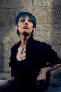 A photo of Maki Yamazaki. She has very short blue hair and is wearing all black. 