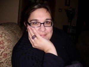A photo of Sonia Allori. She has one of her hands on her face. She has dark brown hair that is tied back and is wearing glasses. 