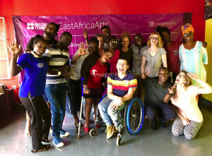A group of 16 people are posing for a photo. The photo has been taken at a training session BOP was running in Rwanda for the British Council. Most of the people are black but there are four white people. One lady is using crutches and Robert from BOP is in his wheelchair, in the centre of the picture (how does he always manage that). Everyone is smiling and some people have their hands raised waving at the camera.