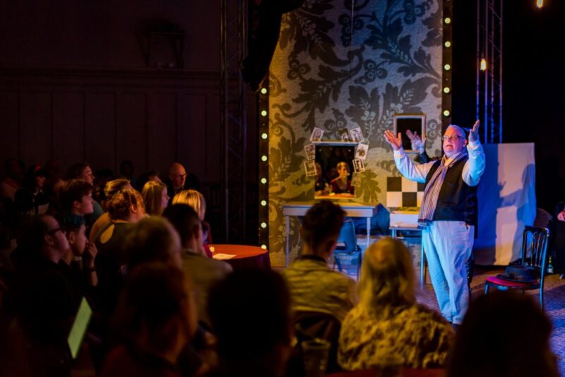 People watch a man talking on stage with his arms in the air