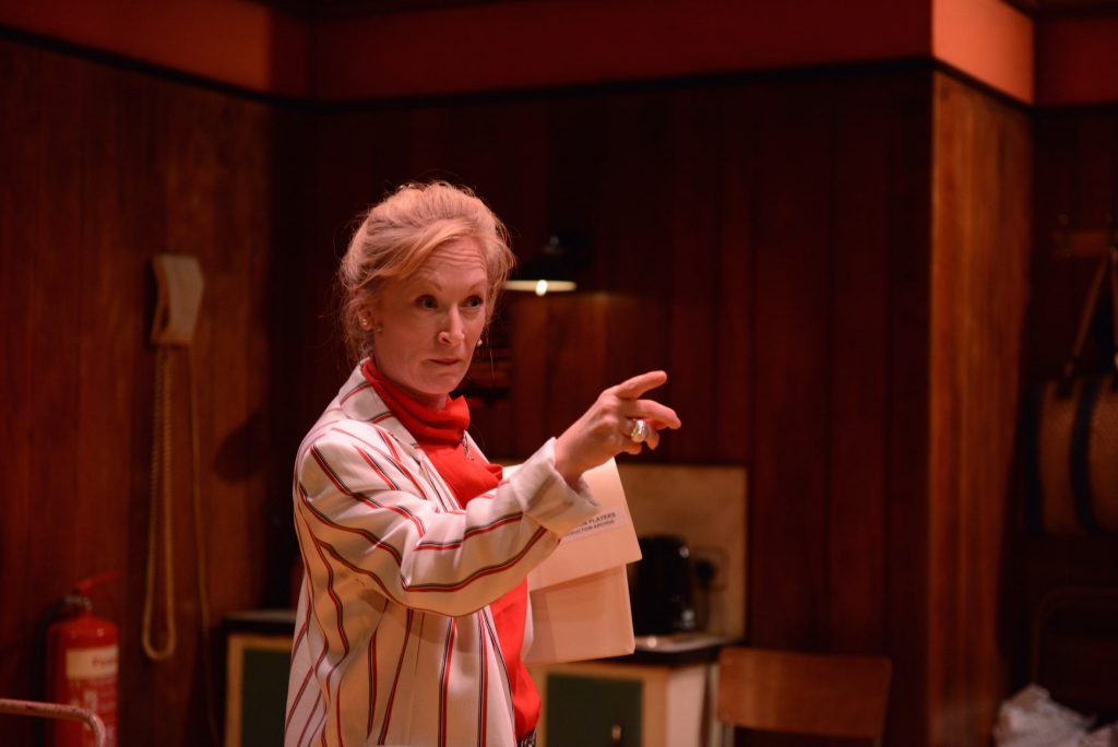 A woman in a stripy jacket and an orange jumper points accusingly at something outside of the picture.
