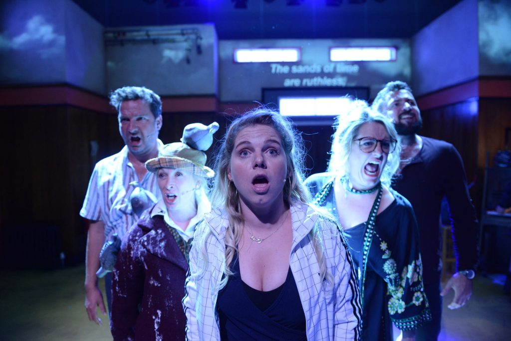 A close up of 5 actors at the front of the stage. They appear to be singing, they all look very serious.