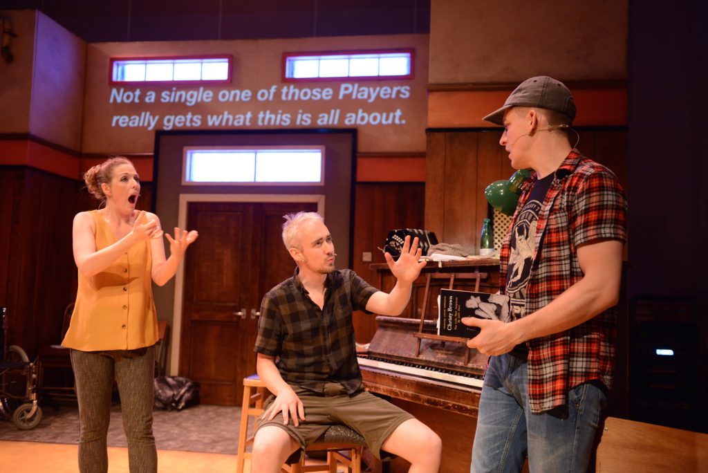 3 actors on stage, They appear to be having a conversation, one of them is signing and one of them sits at a piano