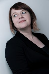 A photo of Emily Reutlinger. She has brown hair that is tied back and is wearing a black blazer. 
