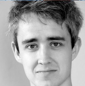 A photo of Gavin Whitworth. He has messy brown hair and thick eyebrows.