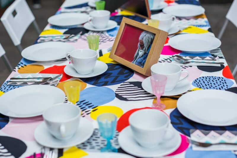 A collection of white cups and saucers on a bright patterned tablecloth.