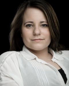 Amy Conachan: Disabled white woman in her 30s, with long brown hair and a half smile on her lips.