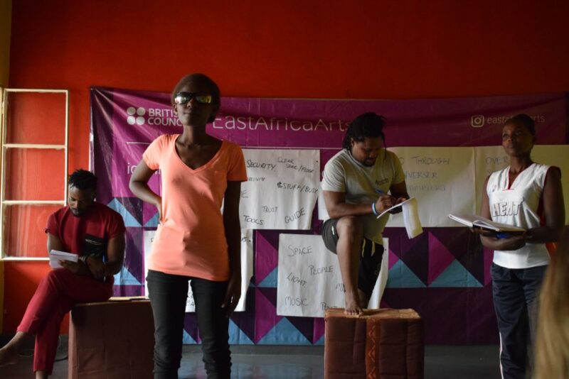 A cropped image of 4 people gathered around with scripts in their hands.