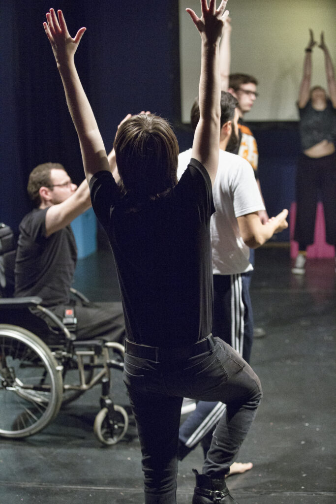 A number of performers participating in a movement exercise - they are stretching upwards, towards the sky.