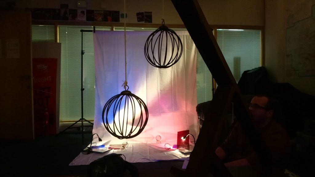 A room, softly lit in pastel colours. Minimalist kinaesthetic decorations hang in the air.