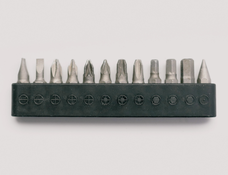 A row of 13 different types of heads for a screwdriver, for all sorts of different types of screw. They are each neatly slotted into a rubber holder.