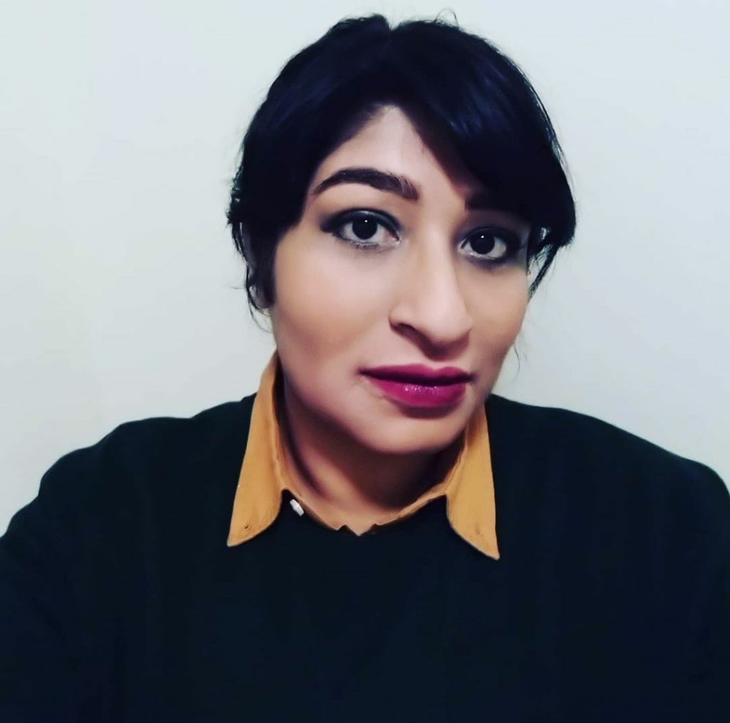 Headshot of Myla: Person of Asian heritage in their early 30s. They wear a black jumper with a yellow collar poking out the top. They have long black hair tied back and wide eyes open and inquisative.