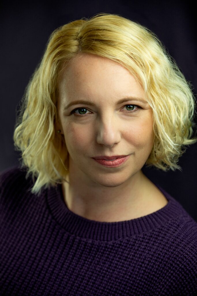 Headshot of Gillian, a white wmon in their 30s. They have a short blond bob, and are giving a slight smile.