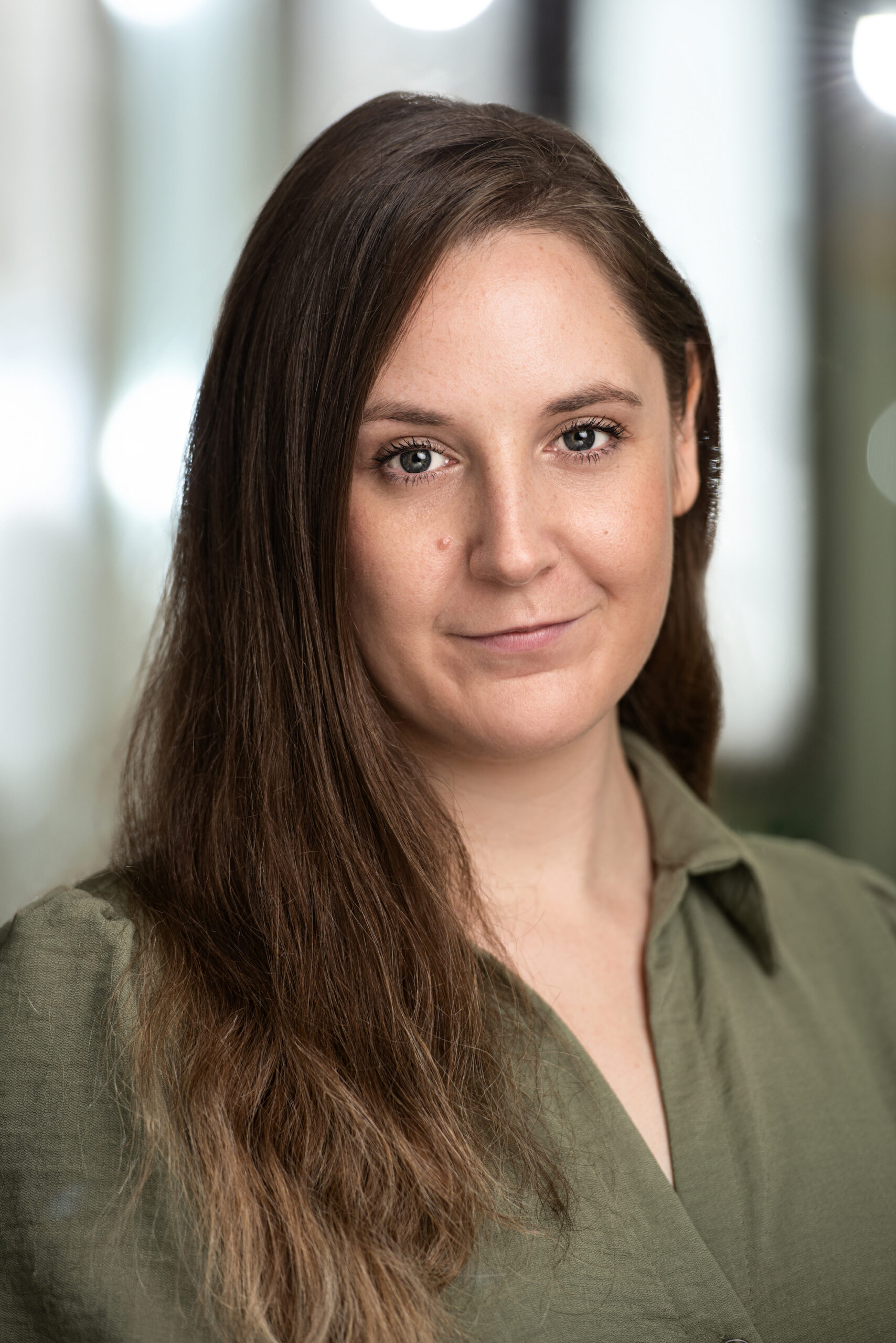 A young woman with long dark hair, wearing a mossy green shirt.